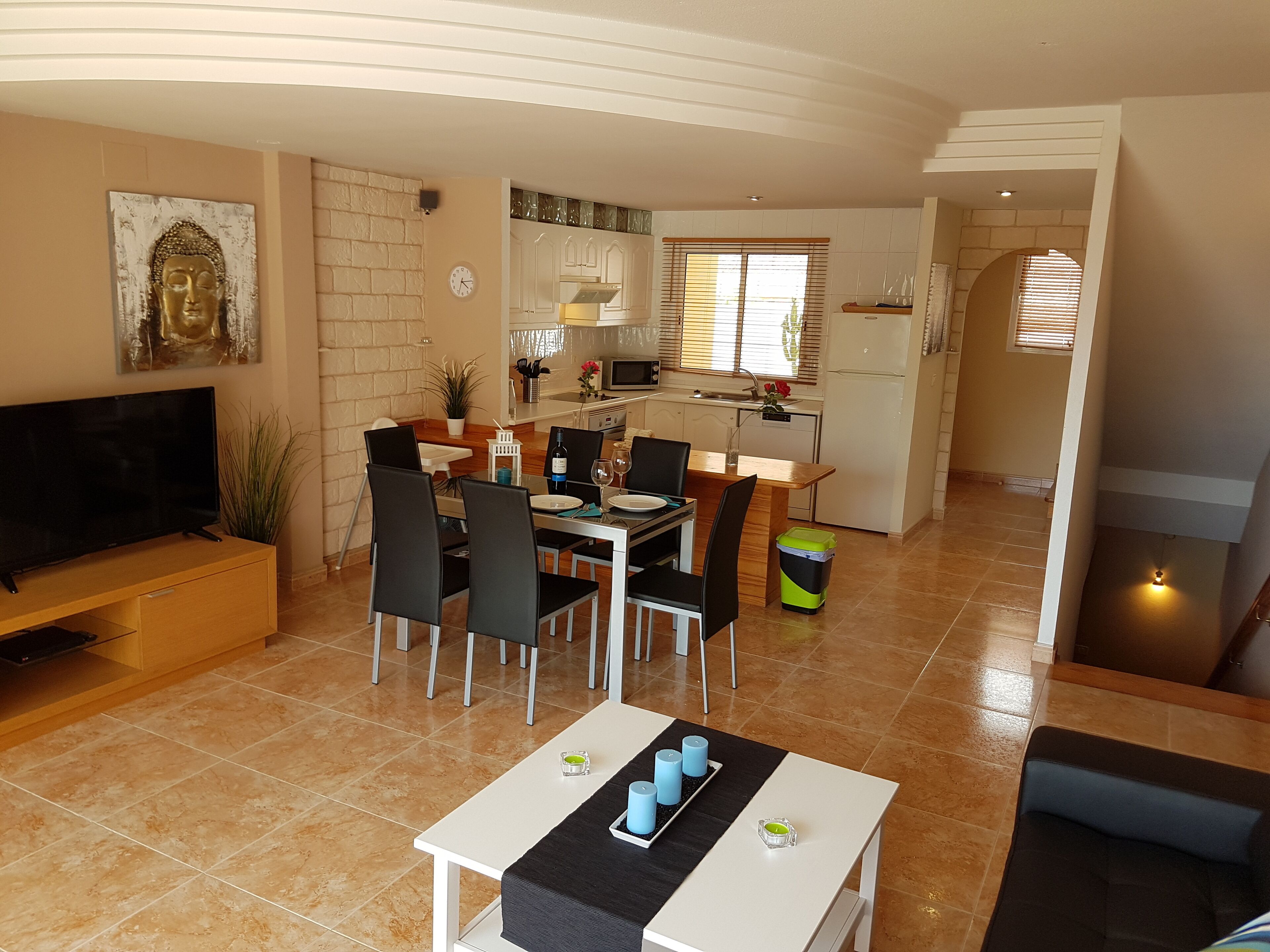 A modern living room with a TV, dining area, kitchen, and a staircase leading to another level.