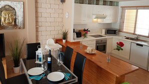 A modern kitchen with white cabinets, a wooden countertop, and a dining area with a table set for two. - Villa Roque del Conde 3 with fantastic sea view, Terrace, Pool, Wifi, SAT-TV (Costa Adeje)
