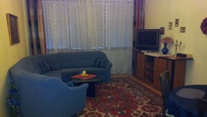 A living room with a blue sofa, a small coffee table, a patterned rug, a television, and a dining table with a chair. - Apartment city center (Wien)