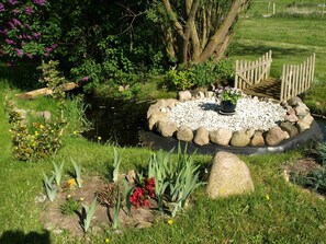 Un jardín con un estanque, rodeado de rocas y diversas plantas.