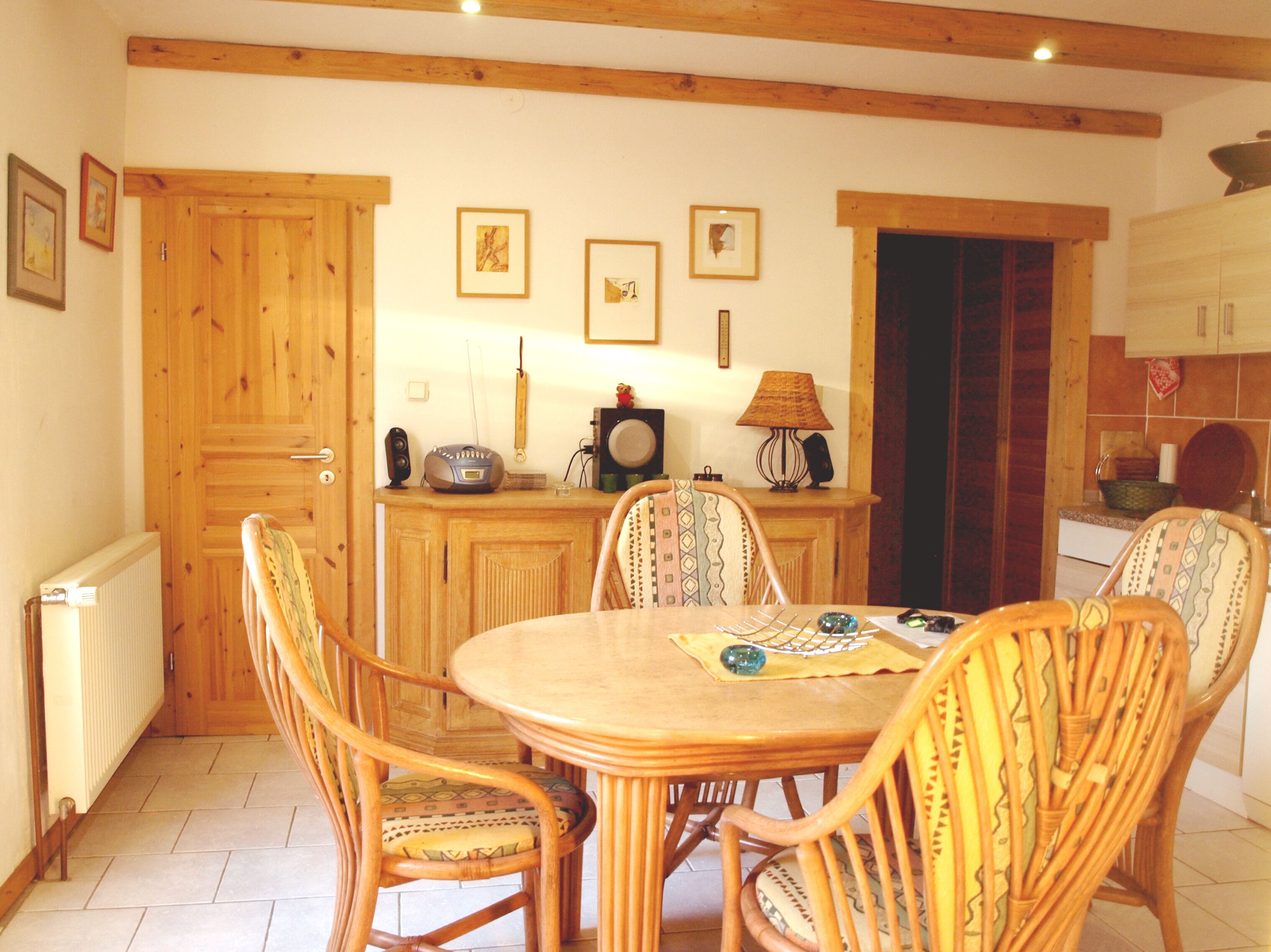 A dining area with a wooden table and chairs, a radio, and framed pictures on the wall.