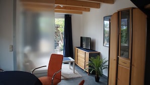 A modern room with a wooden ceiling, a TV on a wooden cabinet, a chair, a table, and a potted plant.
