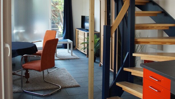 A modern interior with a wooden ceiling, a staircase with blue railings, a dining area with a table and chairs, and a red cabinet.