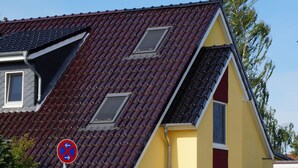 A yellow house with a red roof, a blue sign, and a metal gate.