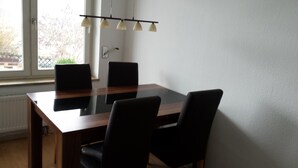 Un espace repas comprenant une table à plateau en verre, des chaises noires et un luminaire suspendu.