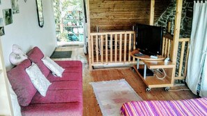 A cozy room with a red sofa, a small wooden TV stand, and a colorful striped bed. - Apartment with flair, quiet location, large garden directly at forest / meadow, large swimming lake at 2km, (Blankenheim-Reetz)