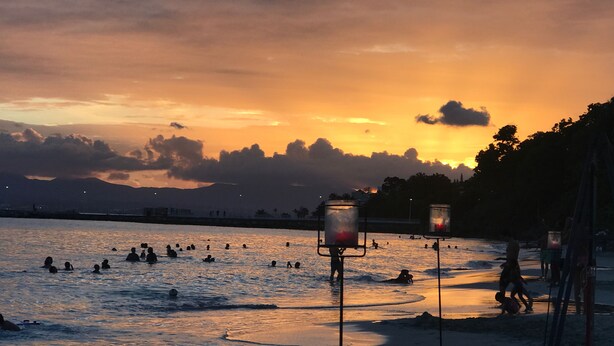 A beach scene with people swimming and playing, and two street lamps in the foreground. - Villa Bois Jolan in Saint-Anne, Guadeloupe (Sainte-Anne)