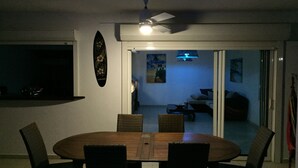 A dining area with a round table and four chairs, a ceiling fan, and a wall-mounted surfboard decoration. - Villa Bois Jolan in Saint-Anne, Guadeloupe (Sainte-Anne)