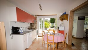 A kitchen with white cabinets, a dining table with a pink tablecloth, and a view of the garden through the glass door. - Gîte de la Bézardais for 4 people in Dinan, Brittany, France. (Quévert)