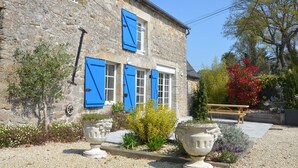 A stone building with blue shutters, a gravel driveway, and a wooden bench. - Gîte de la Bézardais for 4 people in Dinan, Brittany, France. (Quévert)