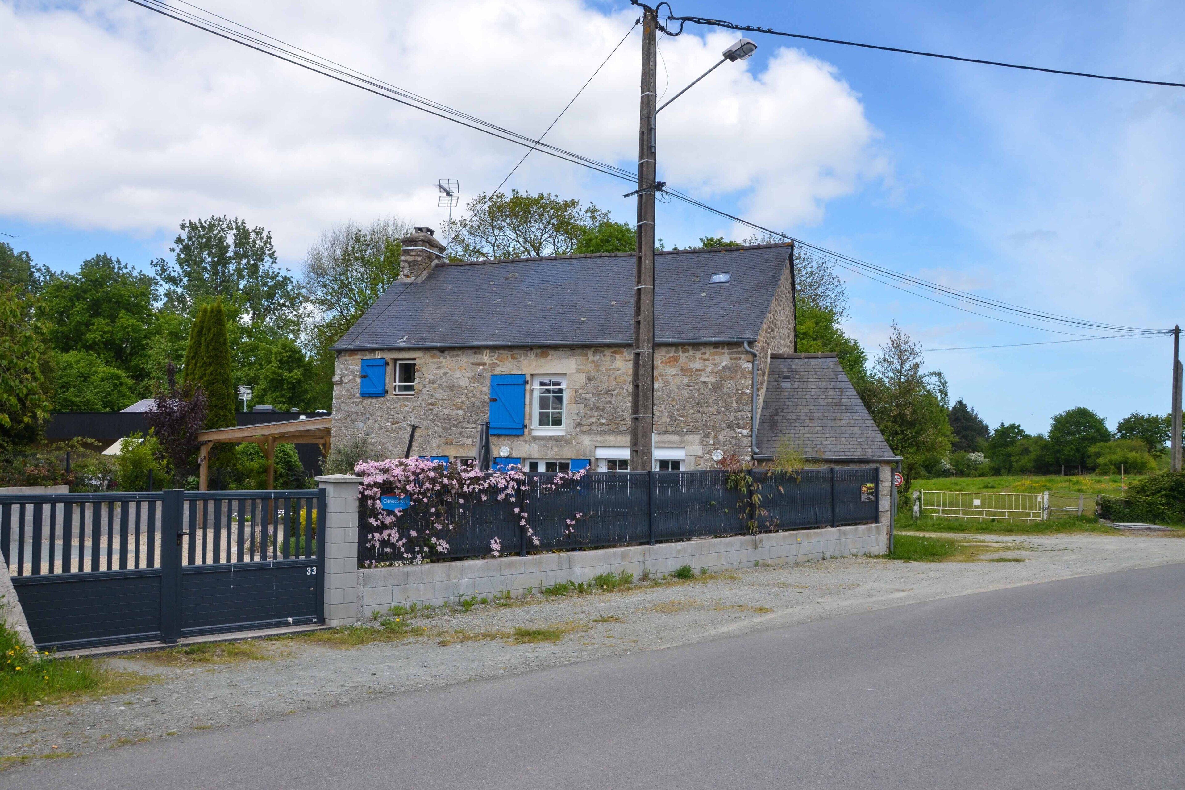 Ein Steinhaus mit blauer Tür und Fensterläden, umgeben von einem schwarzen Zaun und blühenden Pflanzen.