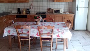 Una cucina con mobili in legno, zoccolo paraschizzi piastrellato, tavolo da pranzo con sedie, microonde e frigorifero.