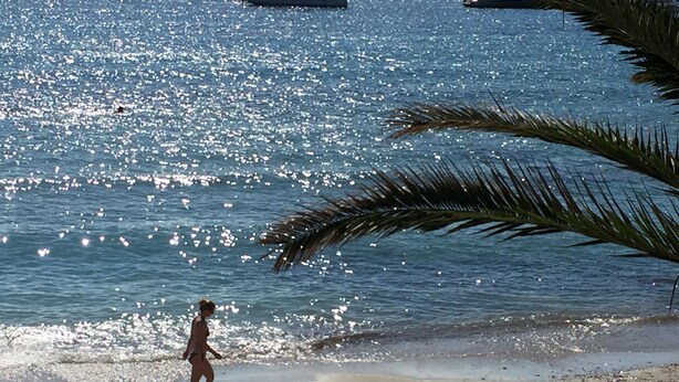 Ein Strand mit Booten im Wasser und einer Person, die am Sand entlanggeht.