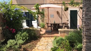 Ein Steinweg führt zu einer Terrasse mit Tisch und Stühlen, umgeben von üppiger Bepflanzung und blühenden Pflanzen.