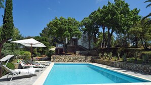 Une piscine entourée de murs de pierre et de verdure, avec des chaises longues et des parasols.