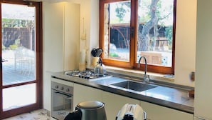 Une cuisine de taille réduite, équipée d’une cuisinière à gaz, d’un évier et d’une fenêtre donnant sur un jardin.