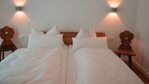 A double bed with white linens, two bedside tables with wooden carvings, and wall-mounted lights. - Family-friendly modern country house (Zell am See)