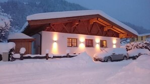 A snow-covered chalet with a wooden roof and a covered porch. - Family-friendly modern country house (Zell am See)