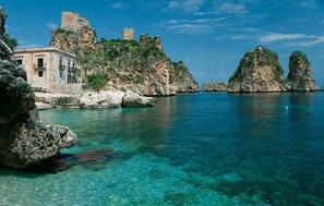 A coastal building with a tower, surrounded by clear blue waters and rocky cliffs. - Posh Villa Carla with private pool, near the beach (Balestrate)