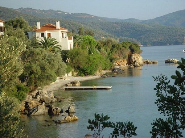 Una casa costera con vista al mar, rodeada de vegetación y colinas.