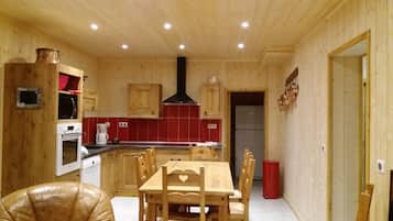 Un interno in legno con un tavolo da pranzo, sedie, angolo cottura con piano cottura, forno e pensili, e un cestino della spazzatura rosso.