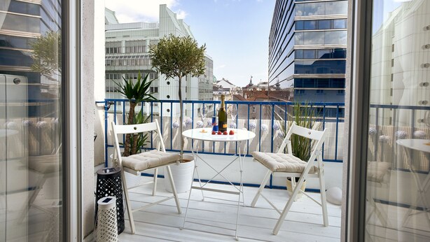 A balcony with white chairs, a small round table, and a bottle of champagne. - STATE OPERA SUITE CITY CENTER "Santorini" (Wien)