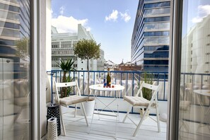 A balcony with white chairs, a small round table, and a bottle of champagne.