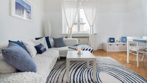 A modern living room with a white sofa, a coffee table, and a view of the city through sheer curtains. - STATE OPERA SUITE CITY CENTER "Santorini" (Wien)