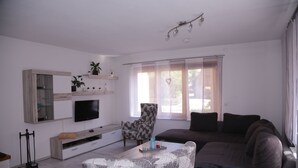 A modern living room with a flat-screen TV, a sofa, a patterned armchair, and a coffee table. - Comfort apartment with open fireplace 3 *** (Kandern)