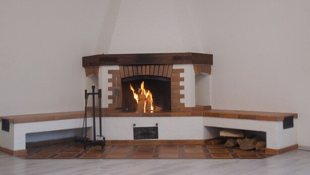 A fireplace with a brick surround and a mantel, with logs stored underneath. - Comfort apartment with open fireplace 3 *** (Kandern)