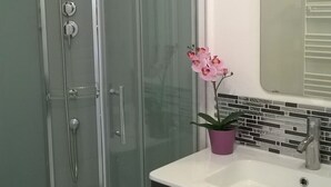 Un baño moderno con ducha de vidrio, un lavamanos blanco con gabinete negro y una orquídea rosa.