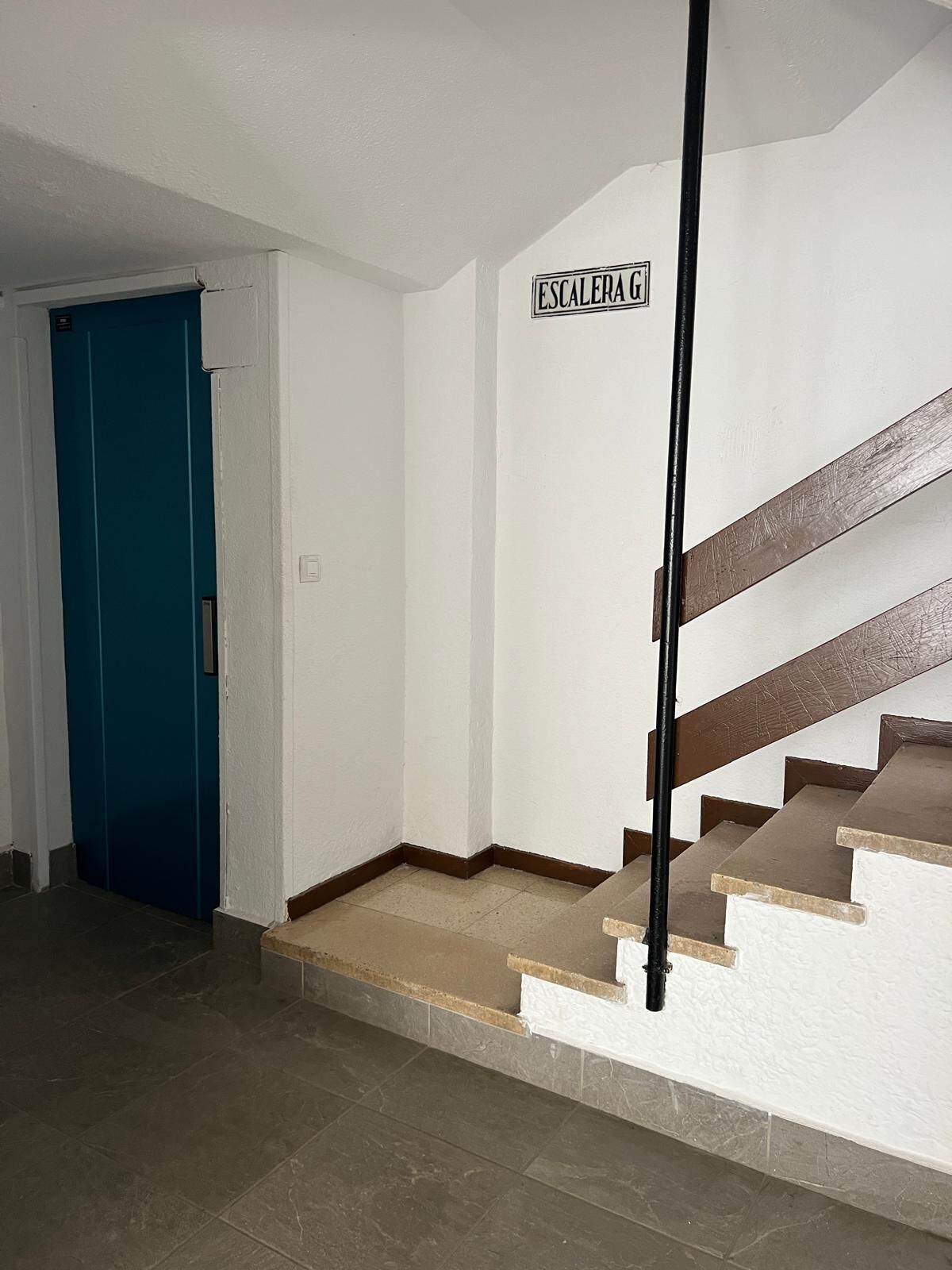 Un escalier avec une pancarte indiquant « ESCALERA G », qui mène à une porte bleue.