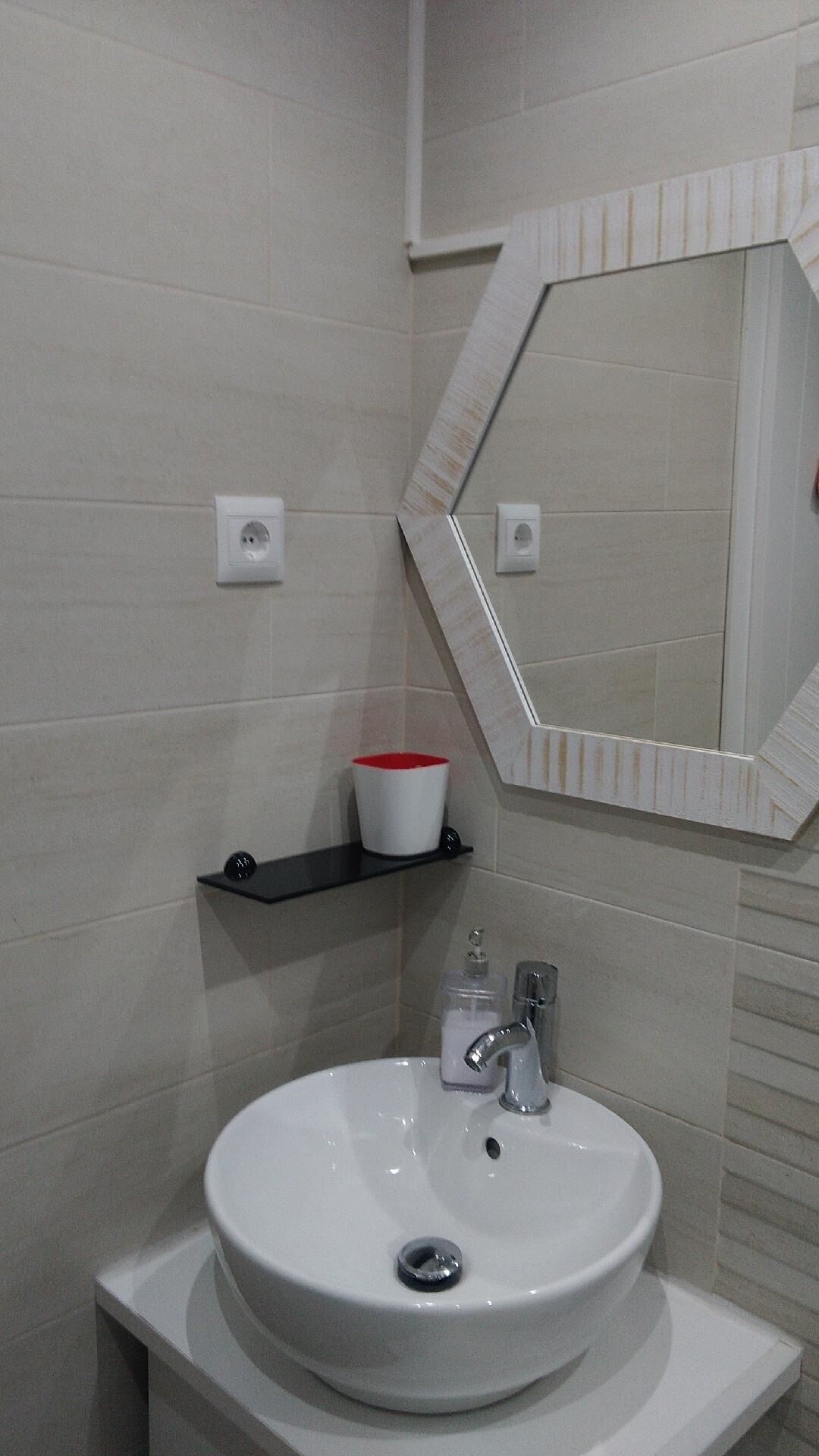 A bathroom with a white sink, a mirror with a geometric frame, and a red and white cup on a black shelf.