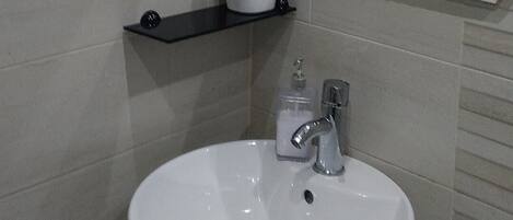 A bathroom with a white sink, a mirror with a geometric frame, and a red and white cup on a black shelf.