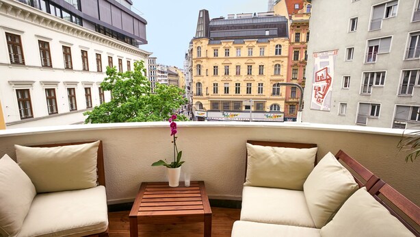 Un balcon avec deux fauteuils rembourrés, une petite table en bois et une plante en pot.