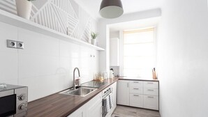 Une cuisine moderne avec des meubles blancs, un plan de travail en bois, un four encastré et une fenêtre qui laisse entrer la lumière naturelle.