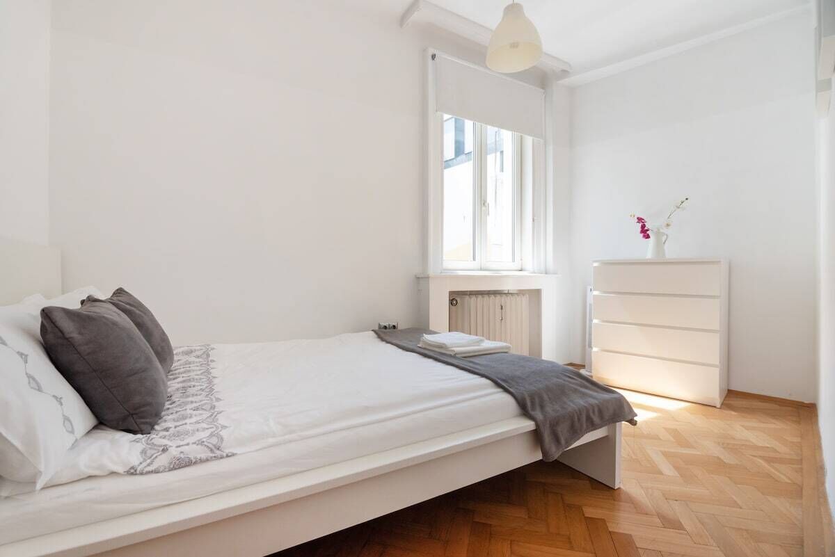 Un dormitorio minimalista con cama, cómoda y radiador.
