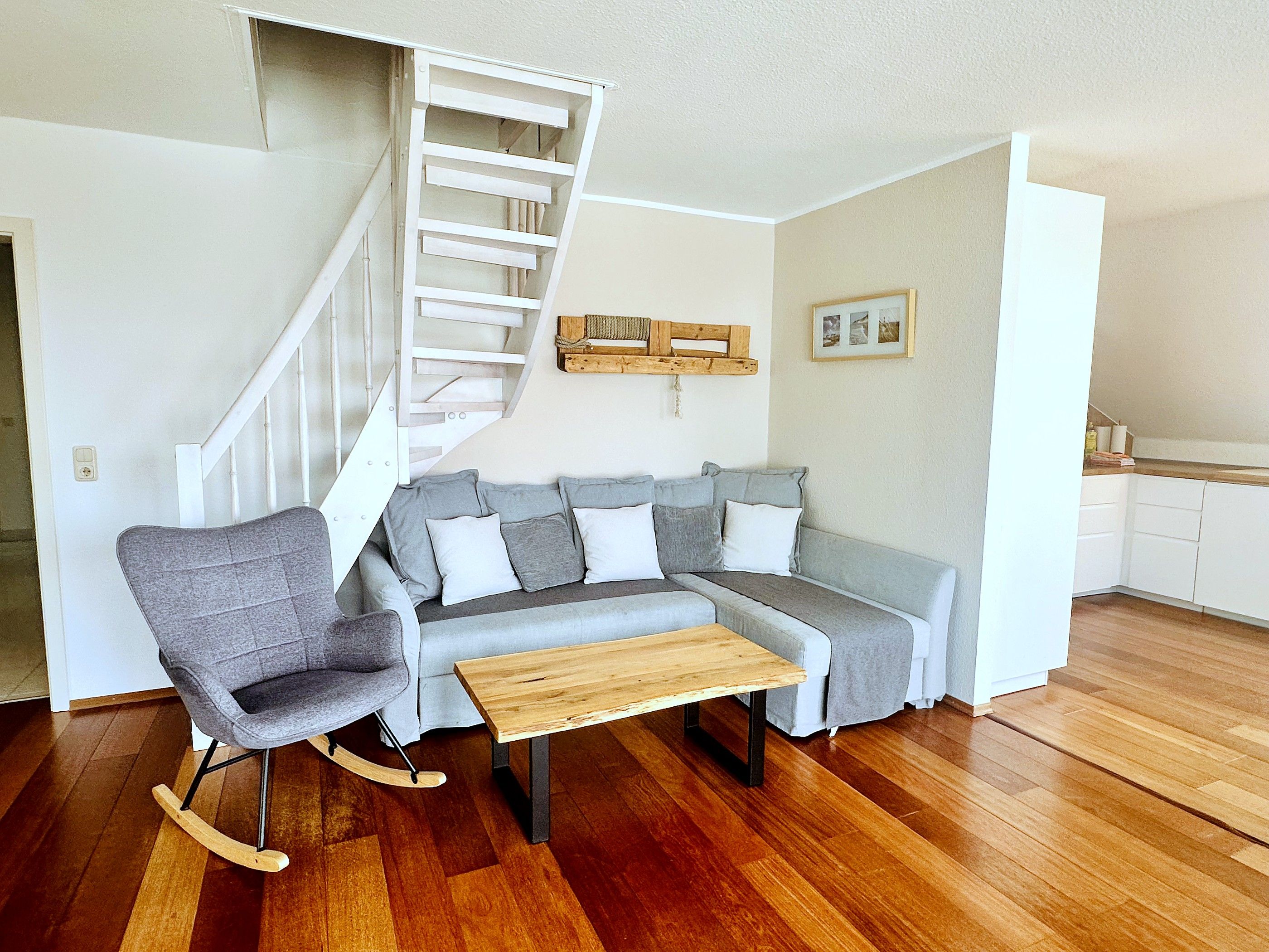 A living room with a grey sectional sofa, a rocking chair, a wooden coffee table, and a white staircase.