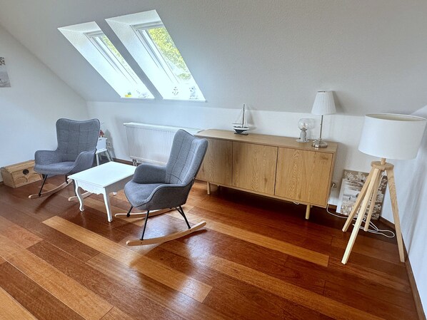 A room with a wooden floor, a rocking chair, a small table, a cabinet, and a lamp.