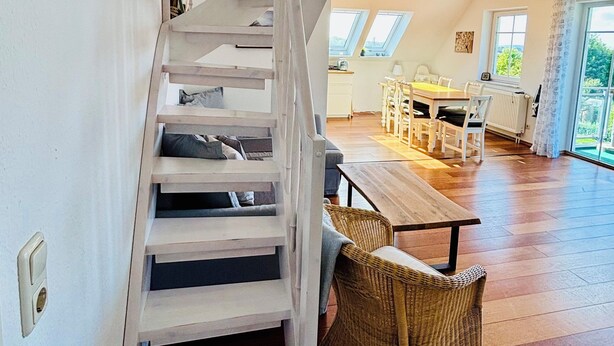 Un vaste espace de vie agrémenté d’un escalier en bois, d’une table à manger et d’un fauteuil en osier.