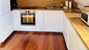 Une cuisine moderne avec des meubles blancs, un plan de travail en bois, un four encastré et une fenêtre au-dessus de l’évier.