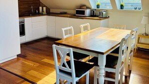 Une cuisine moderne avec une table en bois et des chaises blanches, un four encastré et un four à micro-ondes. Deux puits de lumière naturels illuminent l'espace.