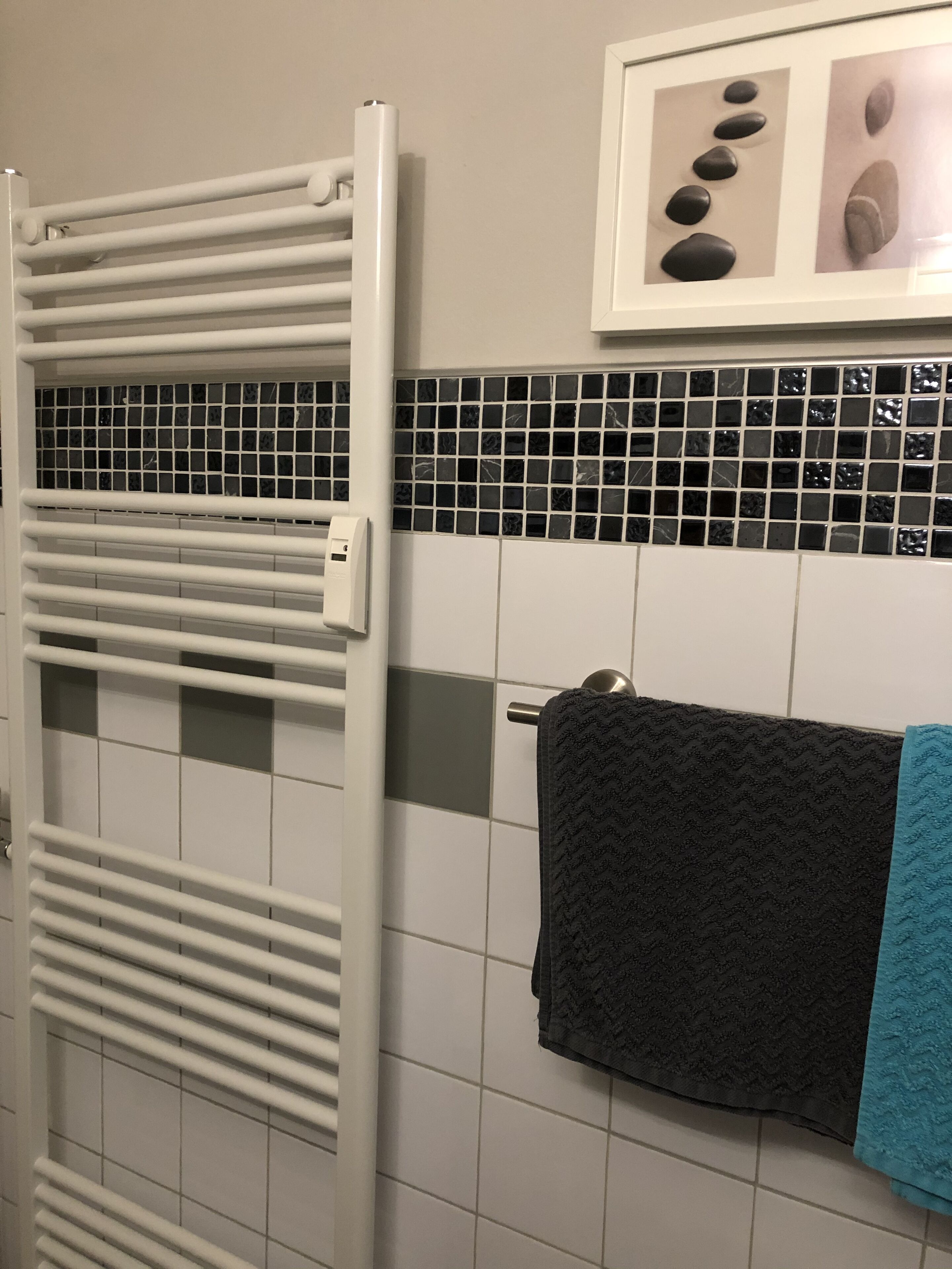 Um banheiro com um porta-toalhas branco, uma toalha preta e uma toalha azul.