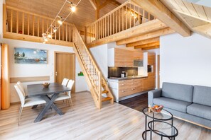A spacious living area with a dining table, grey sofa, and a kitchen in the background. - Comfortable apartment embedded between lake and mountains (Willerzell)