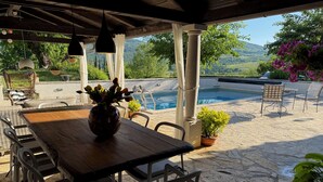 Un espace extérieur abrité, aménagé pour les repas, avec une piscine, un sol en pierre et des plantes en pot.