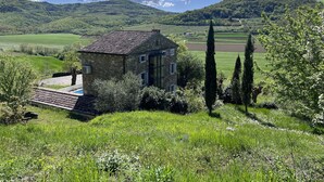 Une maison en pierre avec un toit de tuiles, entourée d’une végétation luxuriante et offrant une vue sur des collines ondoyantes.