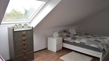 A bedroom with a skylight, a bed with a quilt, a dresser, and a nightstand.