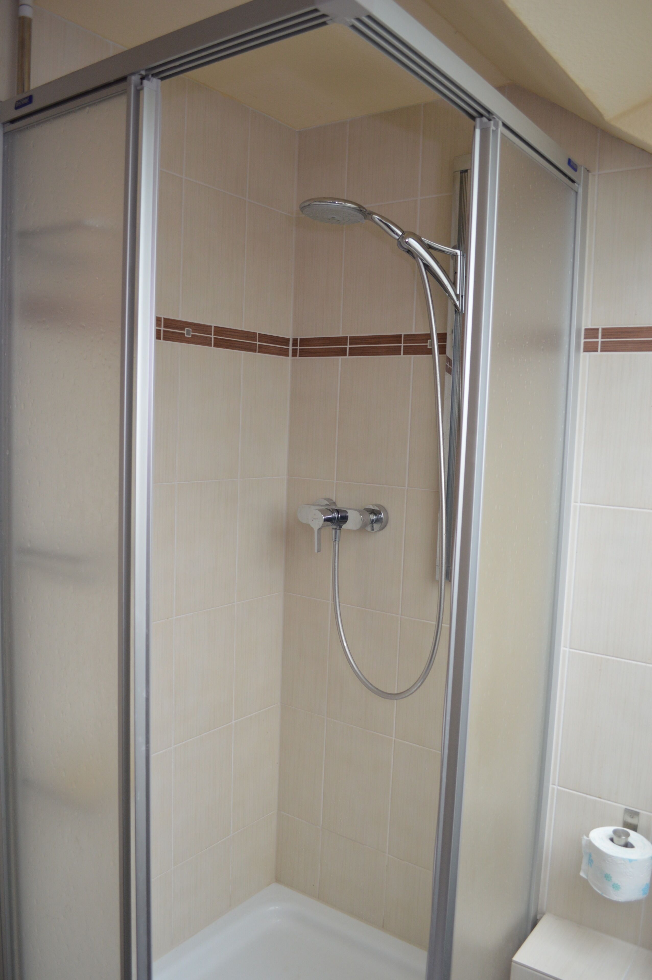 Un box de ducha con puerta de cristal, un cabezal de ducha de mano y un grifo instalado en la pared.