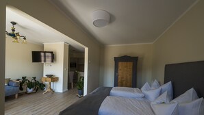 Une chambre avec deux lits, un téléviseur fixé au mur, une porte en bois et une petite table sur laquelle est posée une plante.