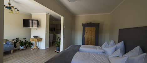 A bedroom with two beds, a TV mounted on the wall, a wooden door, and a small table with a plant.